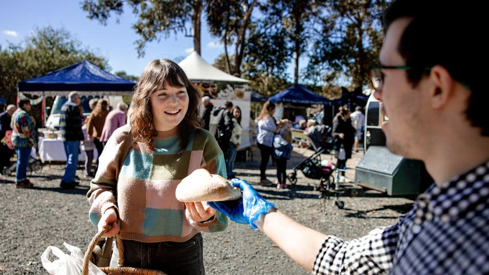 The man is also wearing blue food handlers gloves and the woman has a woven basket in her other hand