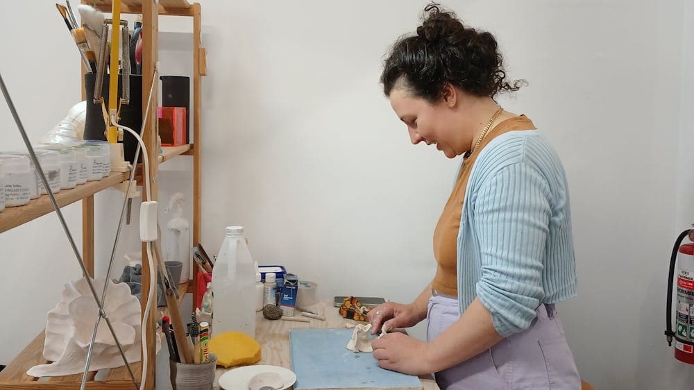 Side view of young woman standing up and working on a ceramic piece.ic p