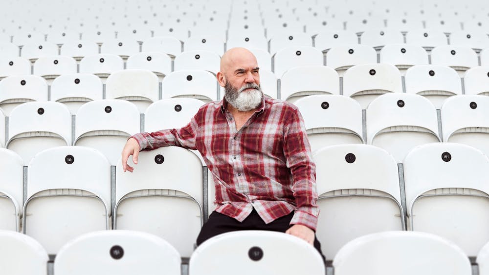 Marty Sheargold in a flannel shirt seated in a stadium with white chairs