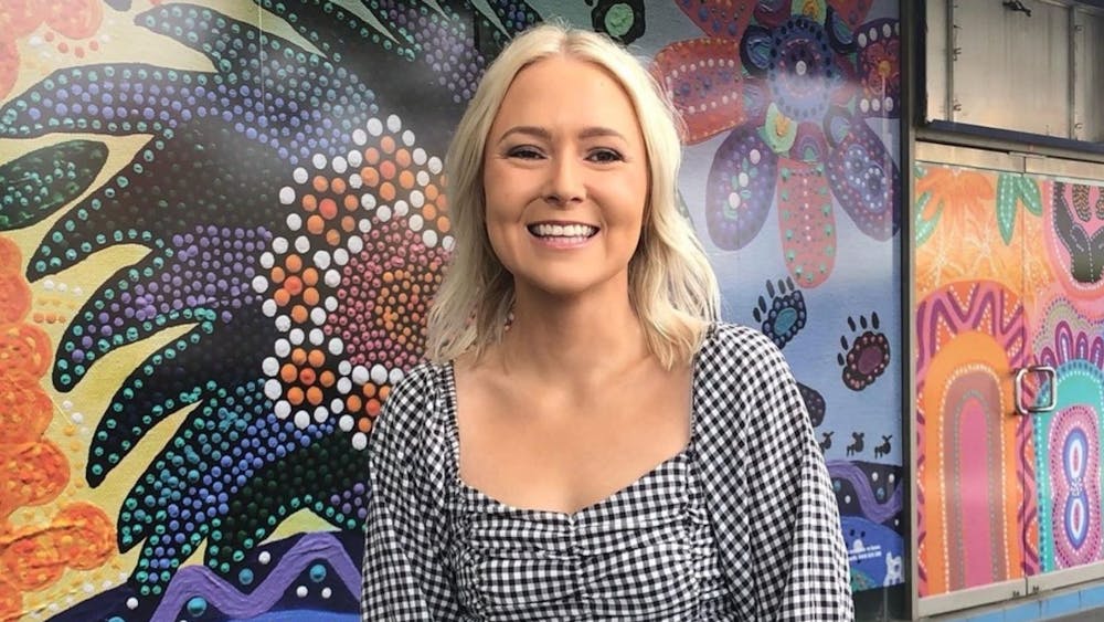 Artist Jenna Oldaker standing in front of her indigenous artwork